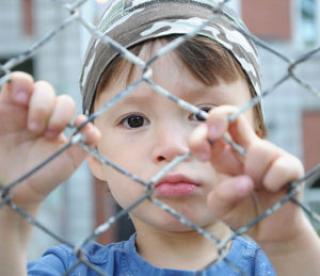 caucasian boy looking sadly through the bars outdoor