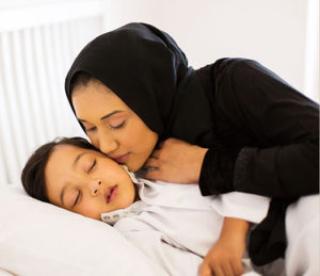 caring muslim mother kissing baby boy while he is asleep