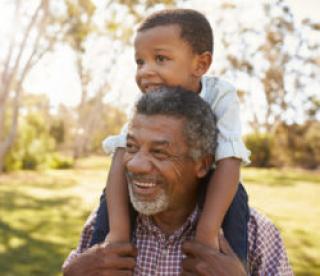 Grandfather Carries Grandson On Shoulders During Walk In Park 