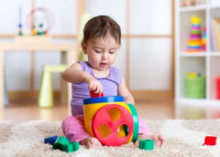 Toddler sitting on floor playing with a sorter toy 