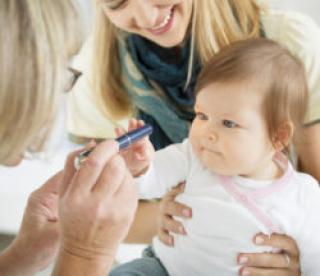 Mother holding her cute baby girl while pediatrician doing an eyesight test with diagnostic light pen. Selective focus to cute baby.