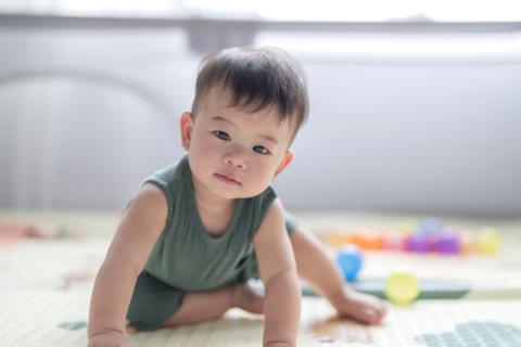 Small Asian American child looking into camera in a green tanktop. 